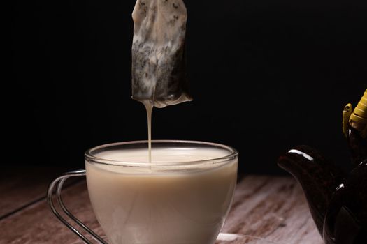 tea cup and teapot pouring a cloud of hot milk on a wooden table