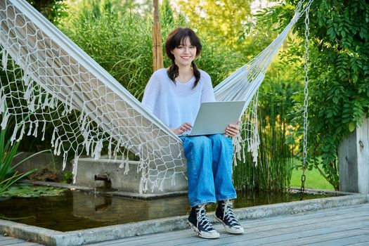 Teenage girl relaxing in hammock using laptop for leisure study
