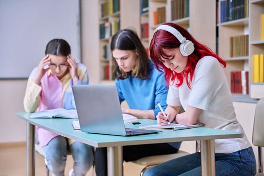 Group of teenage students study at their desks in library class