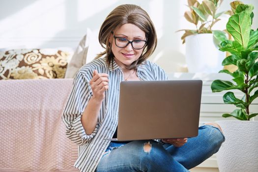 Mature woman using laptop for conference video call, sitting at home