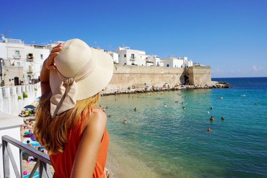 Rear view of young woman with hat and dress enjoying seascape in Monopoli town, Bari, Italy