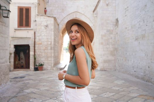 Portrait of smiling attractive tourist woman walking alone in the medieval town of Barletta, Apulia, Italy