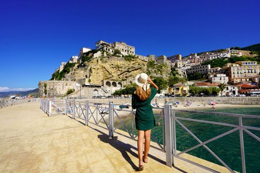 Holidays in Pizzo Calabro, Italy. Back view of beautiful fashion girl enjoying view of the fortress of Pizzo, Calabria. Summer vacation in Italy.