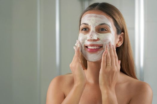 Close-up portrait of attractive woman with a clay mask on face in the bathroom