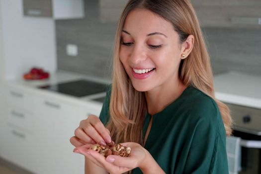 Beauty healthy woman picking mix of nuts dried fruits from her hand at home