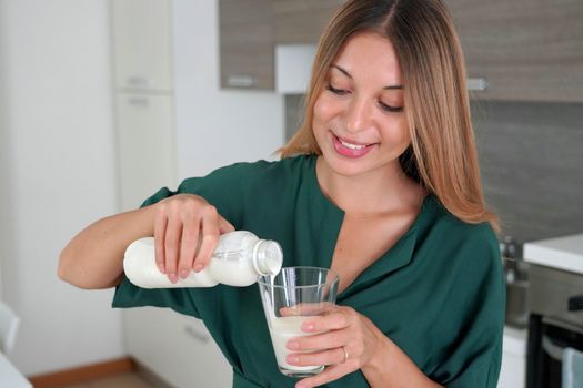 Morning portrait of young smiling woman fills the glass with kefir. Beautiful girl drinking milk.