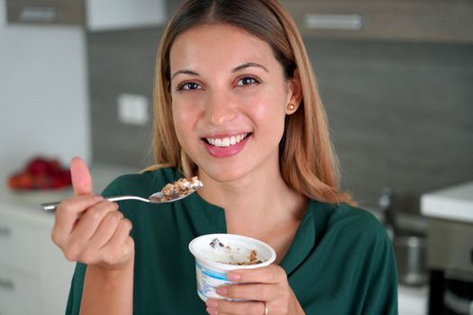 Beautiful young woman eating greek yogurt with muesli at home