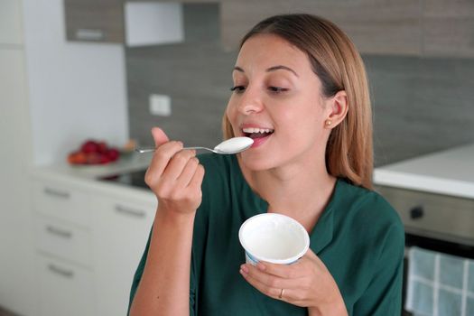 Beautiful young woman eating Greek yogurt from container at home