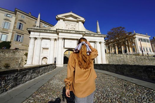 Young tourist woman walking towards Bergamo Porta San Giacomo gate, UNESCO World Heritage Site, Bergamo, Italy