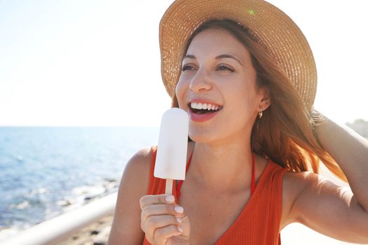 Close-up of beautiful girl with hat holding a white popsicle on the beach looking to the side