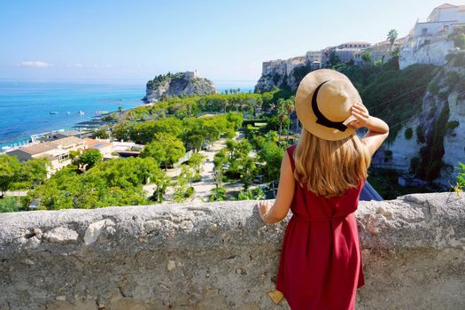Summer holiday in Italy. Back view of young woman with hat and dress enjoying landscape in Tropea village, Calabria, Italy.