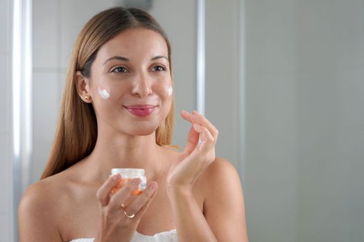 Skincare woman applying cream on her cheek. Face moisturizing nourishing invigorating treatments. Enjoying relaxing time.