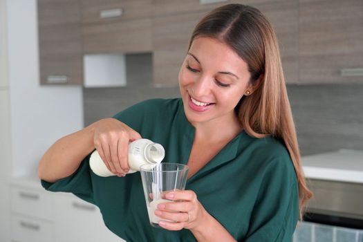 Beautiful girl filling the glass with kefir at home