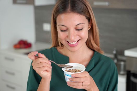 Sweet woman holds bowl of Greek yogurt with muesli in the kitchen 