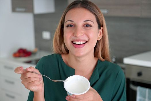 Beautiful girl holds bowl on Greek yogurt in her hand and smiles at camera indoors