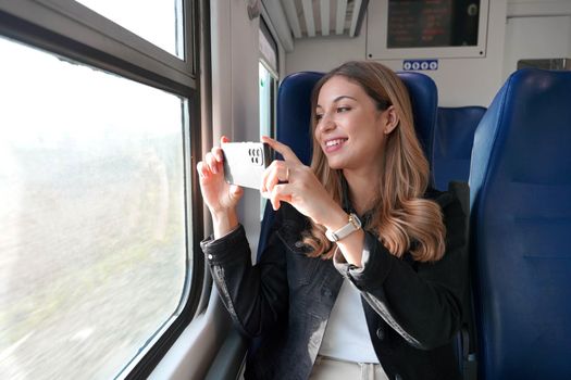 Beautiful girl takes picture of landscape with her smartphone sitting on train