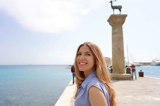 Close-up of happy girl with deer statue landmark of Rhodes city in Greece