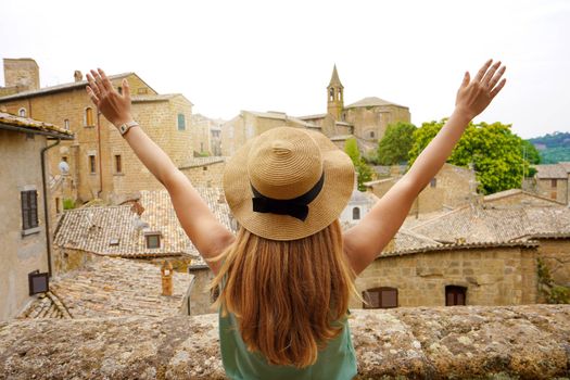 Happy young woman with arms up in Orvieto city. Traveler girl with arms outstretched raised on the town. Tourist on travel holiday in central Italy.