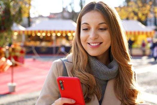 Close-up of young smiling beautiful woman using smartphone on the street at winter
