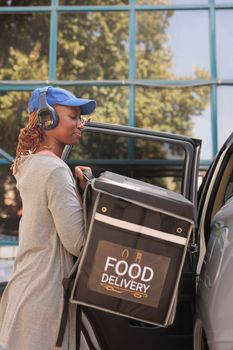 Young courier in headphones delivering restaurant food by car
