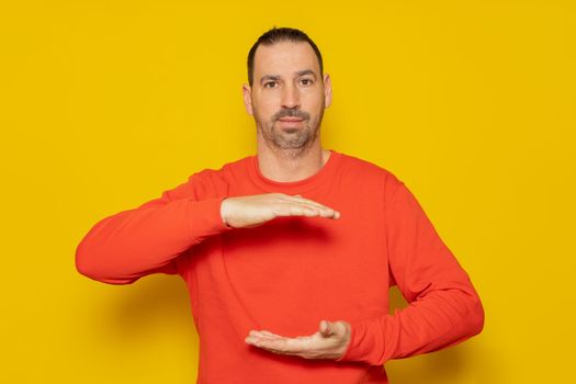 A man holding an object between his hands, showing, offering or advertising an object against an orange wall. Empty. Space. Concept. Object. Bottom. Portrait. Copy