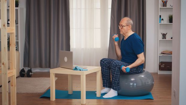 Senior man training biceps watching online fitness lesson. Old person pensioner healthy training healthcare sport at home, exercising fitness activity at elderly age