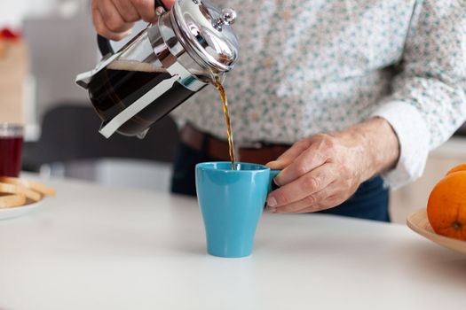 Retired man holding blue cup on table pouring aromatic drink from coffee machine