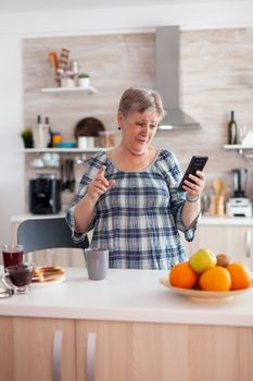 Enthusiastic senior woman speaking on mobile phone webcam with family