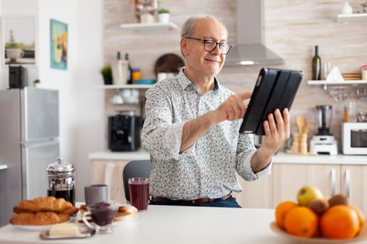 Happy senior man searching on tablet in kitchen during breakfast