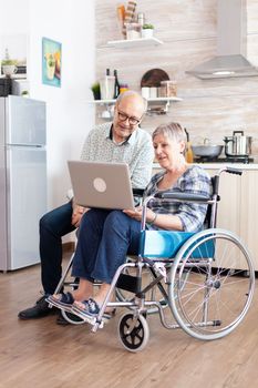 Handicapped senior woman in wheelchair and her husband searching on laptop