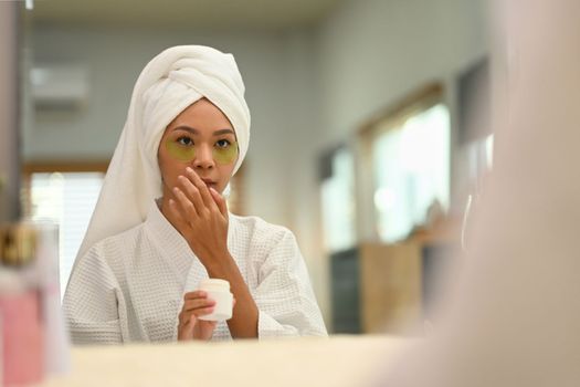 Gorgeous woman in bathrobe using under eye patches, doing morning routine after shower. Self care and daily beauty routine