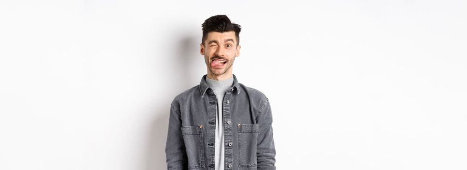 Funny guy with moustache showing tongue and winking, making you laugh, standing on white background