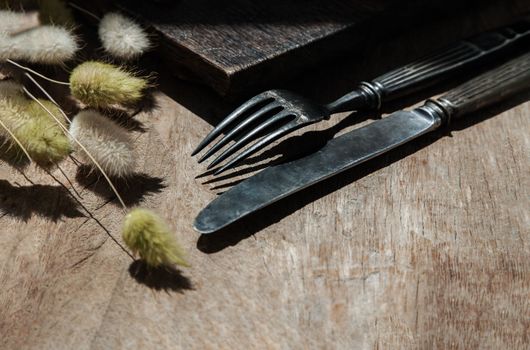 Vintage old metal knife with fork and Dried rabbit tail grass flowers on old rustic wooden table. Eating concept, Copy space, 