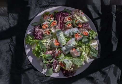 Healthy vietnamese spring rolls with fresh vegetables and lime slices on round ceramic tray.