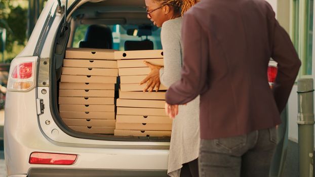 Pizzeria employee giving piles of pizza boxes to diverse clients