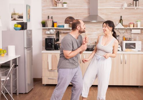 Carefree couple dancing and singing in kitchen