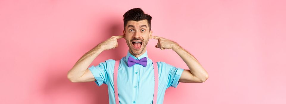 Childish funny guy shut ears and laughing at camera, refuse to listen, standing ignorant on pink background
