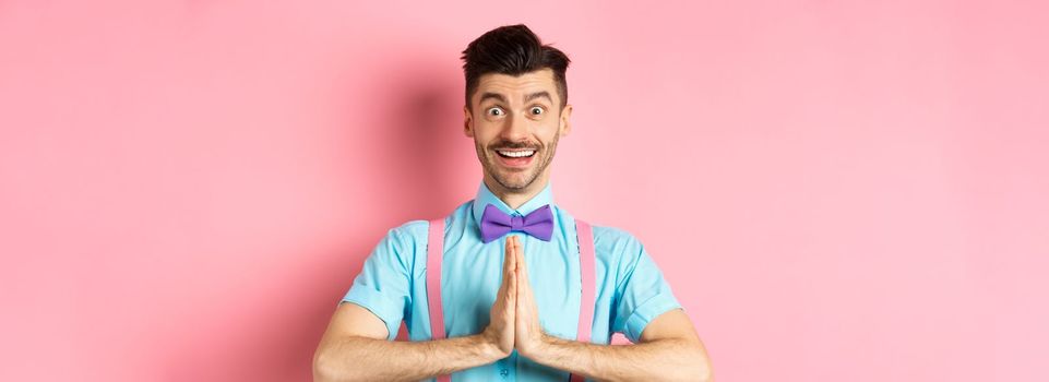 Image of smiling young man asking please, looking grateful at camera, Guy in bow-tie say thank you, standing over pink background