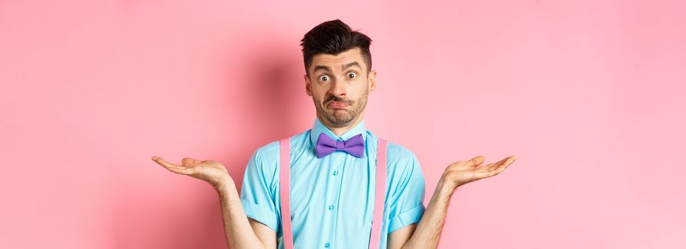 Image of confused guy in bow-tie and suspenders know nothing, shrugging shoulders and looking clueless, standing over pink background