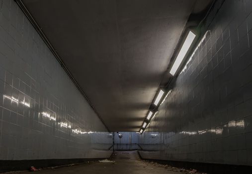 Perspective view of Ambient public underpass with white tiled walls and stripes of ceiling neon lights. 