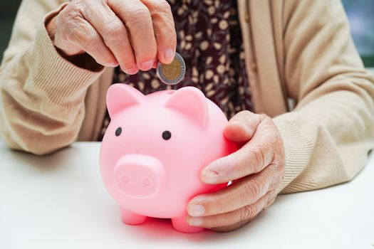 Retired elderly woman putting coins money in piggy bank and worry about monthly expenses and treatment fee payment.