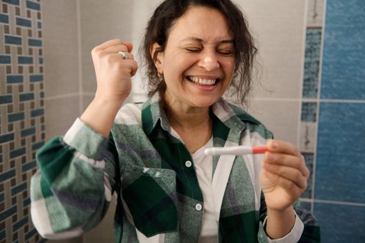 Finally pregnant. Charming multi-ethnic woman rejoicing at positive pregnancy test.