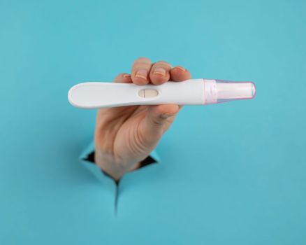 A hand with a negative pregnancy test sticking out of a hole in a blue cardboard background.