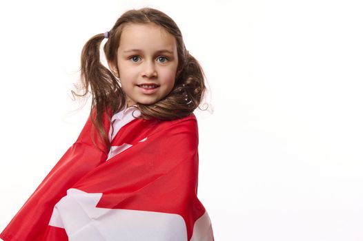 Close-up American citizen, little child girl wrapping in Canadian flag, over white background. Canada Independence Day