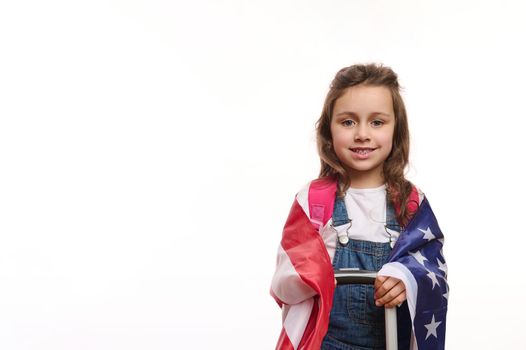 Little American girl with US flag and suitcase, isolated over white background with free space for your promotional text