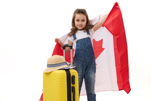 Little child girl carries Canadian flag and suitcase. Concept of study in Canada, emigration, learning foreign languages