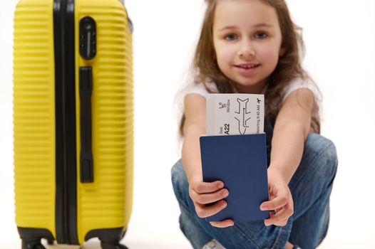 Details: boarding pass and identity documents for travel abroad in hands of a little girl traveller with yellow suitcase