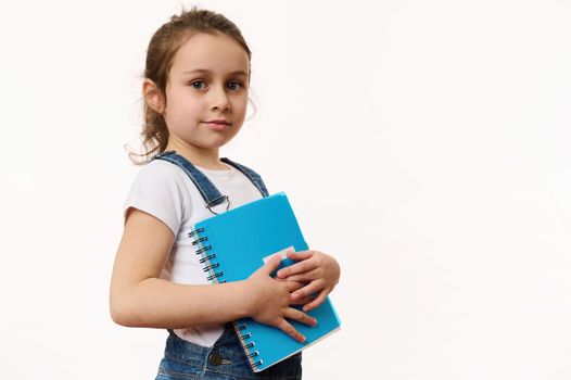 Adorable child, preschooler girl in white t-shirt and blue casual denim with a copybook, isolated on white background