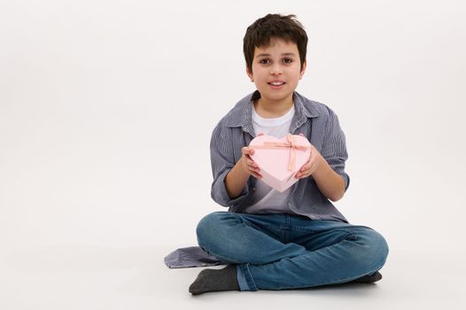 Adorable Middle-Eastern teenage boy holds a beautiful pink heart shaped gift box, isolated on white background