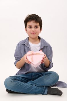 Handsome smiling boy with a cute present for Valentine's Day, Mother's Day or Women's Day, in heart-shaped pink gift box